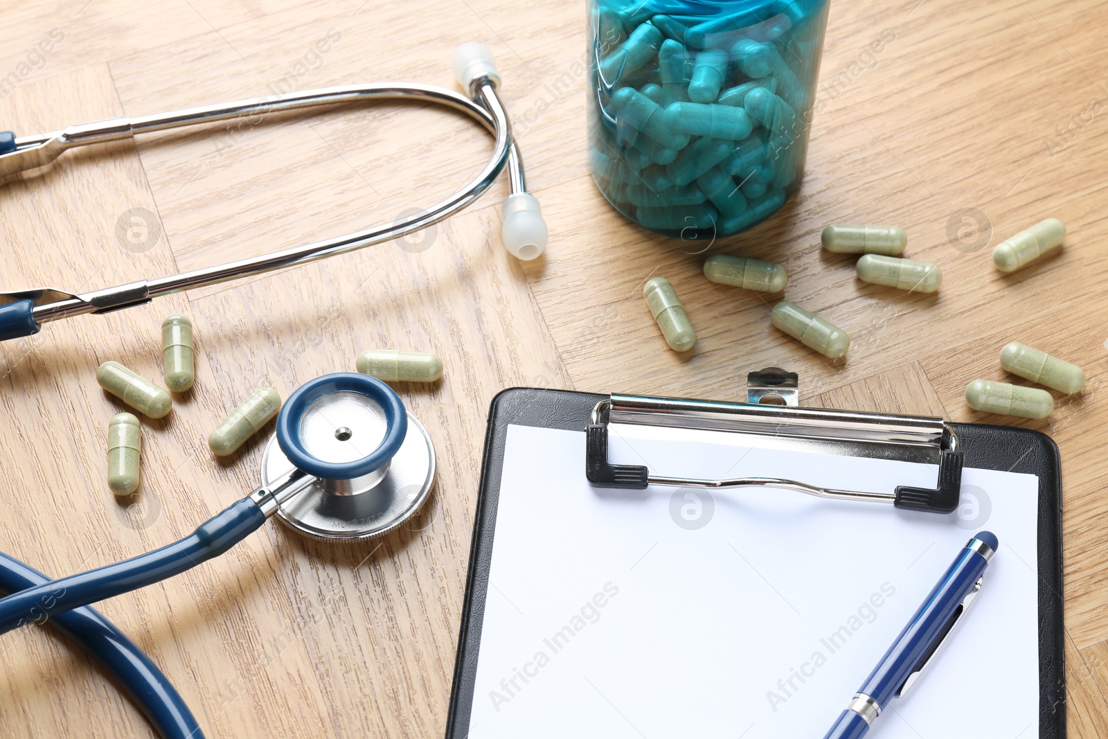 Photo of Pharmacist. Many pills, stethoscope, clipboard and pen on wooden table