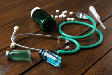 Photo of Pharmacist. Glass vials, stethoscope, plastic bottle, syringe and pills on wooden table, closeup