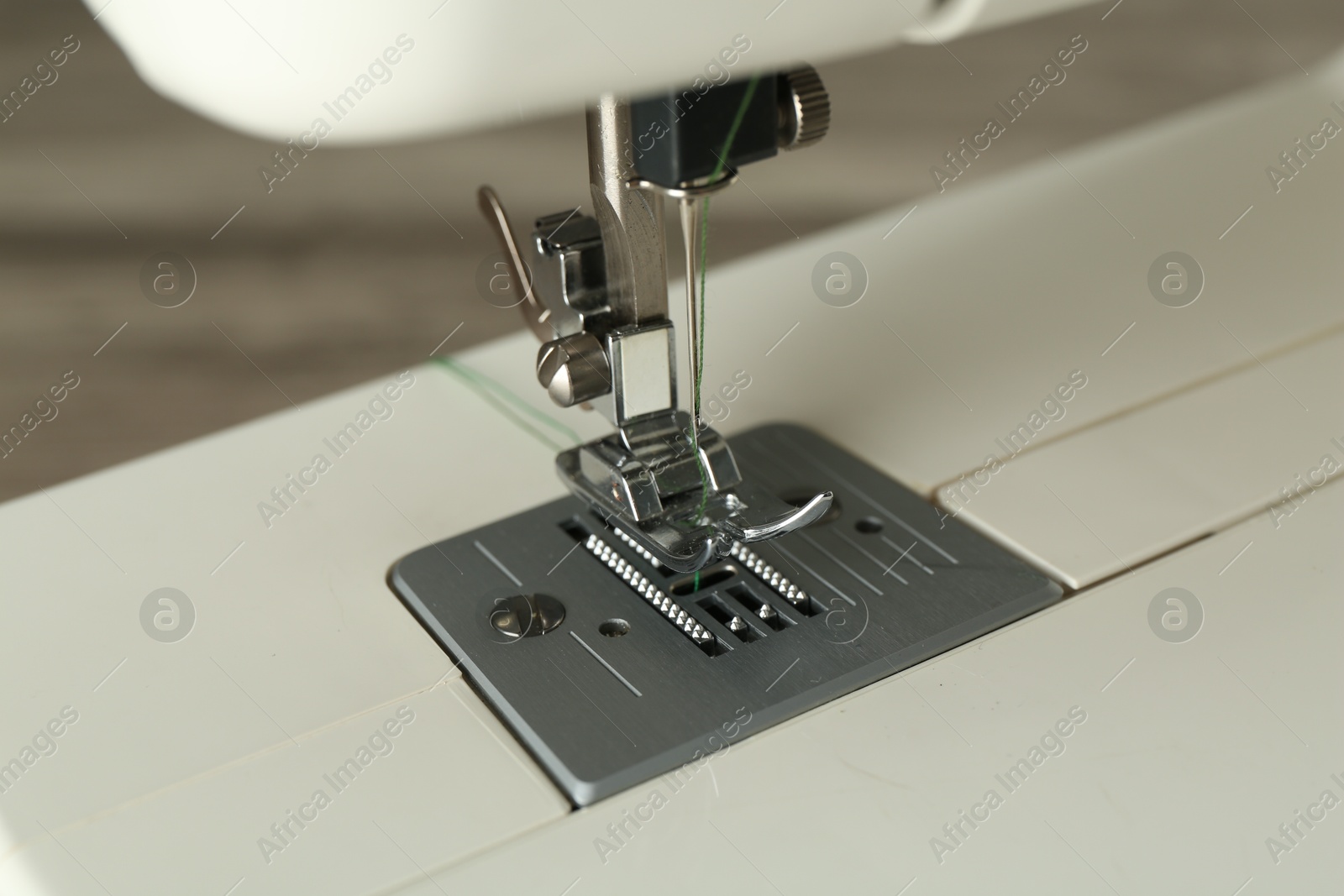 Photo of Sewing machine with green thread on grey background, closeup