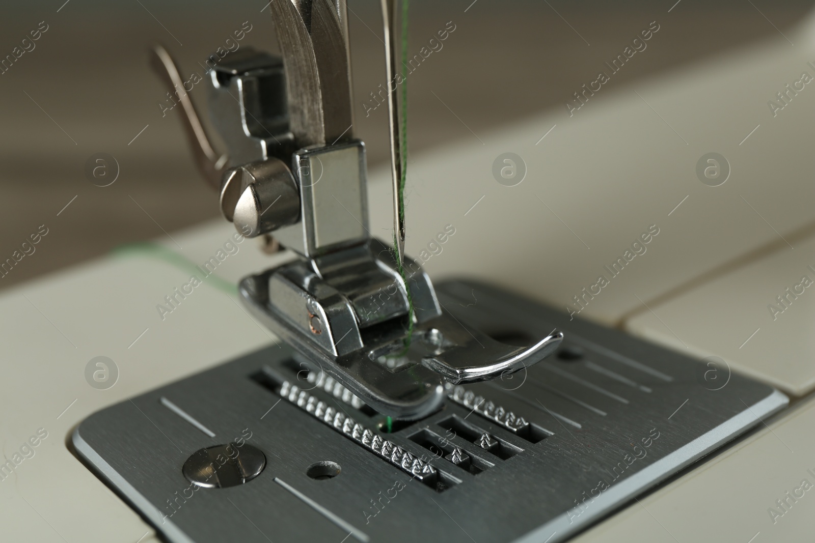 Photo of Sewing machine with green thread on grey background, closeup