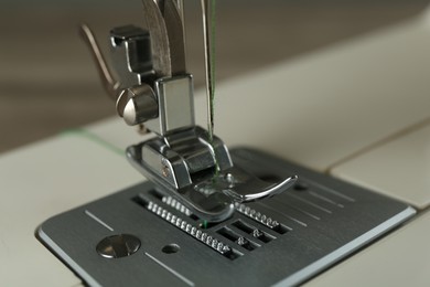 Sewing machine with green thread on grey background, closeup