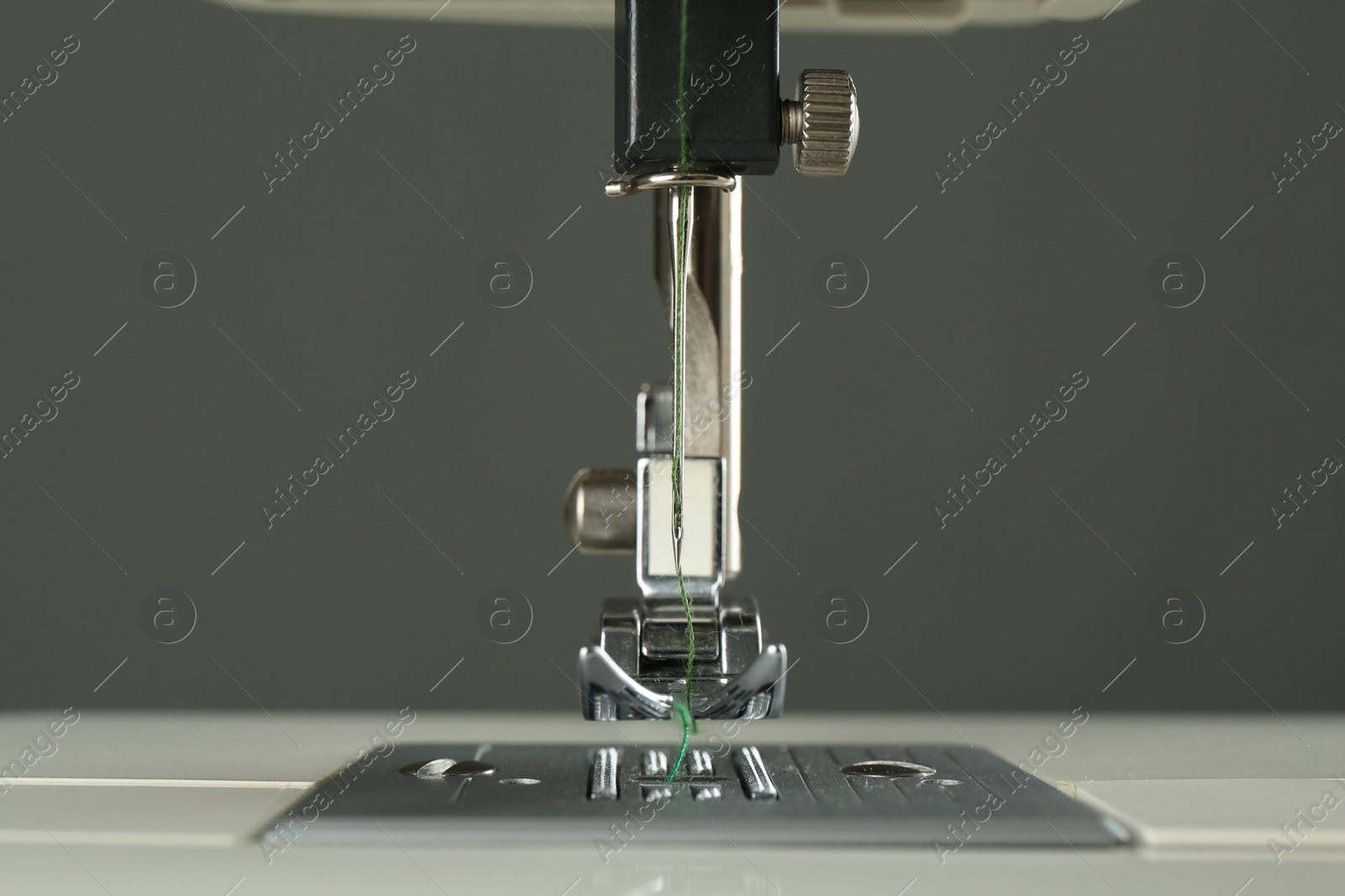 Photo of Sewing machine with green thread on grey background, closeup