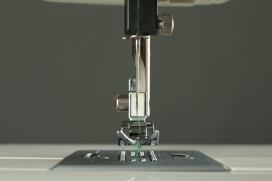 Sewing machine with green thread on grey background, closeup