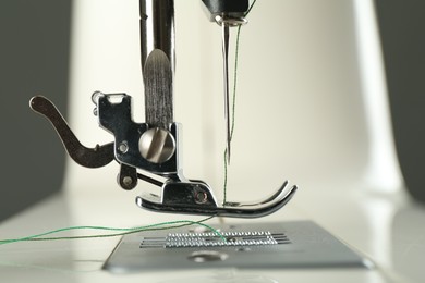 Photo of Sewing machine with green thread on grey background, closeup