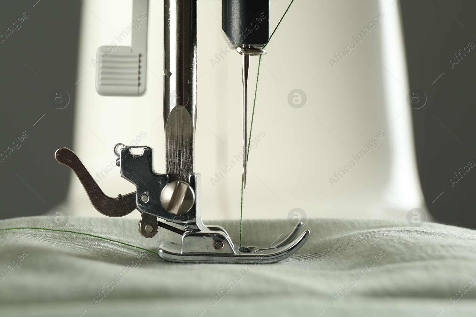 Photo of Sewing fabric with machine on grey background, closeup