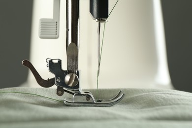 Sewing fabric with machine on grey background, closeup