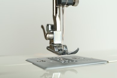 Sewing machine with beige thread on light background, closeup