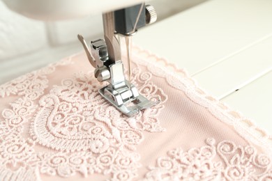 Sewing fabric with machine indoors, closeup view