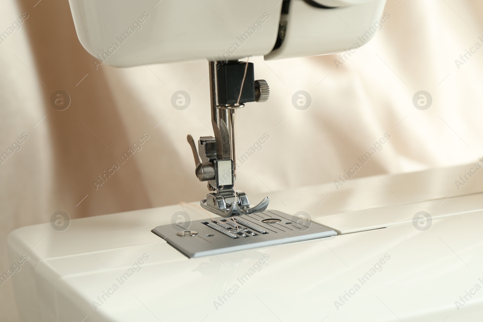 Photo of Sewing machine with beige thread on blurred background, closeup