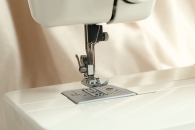 Sewing machine with beige thread on blurred background, closeup