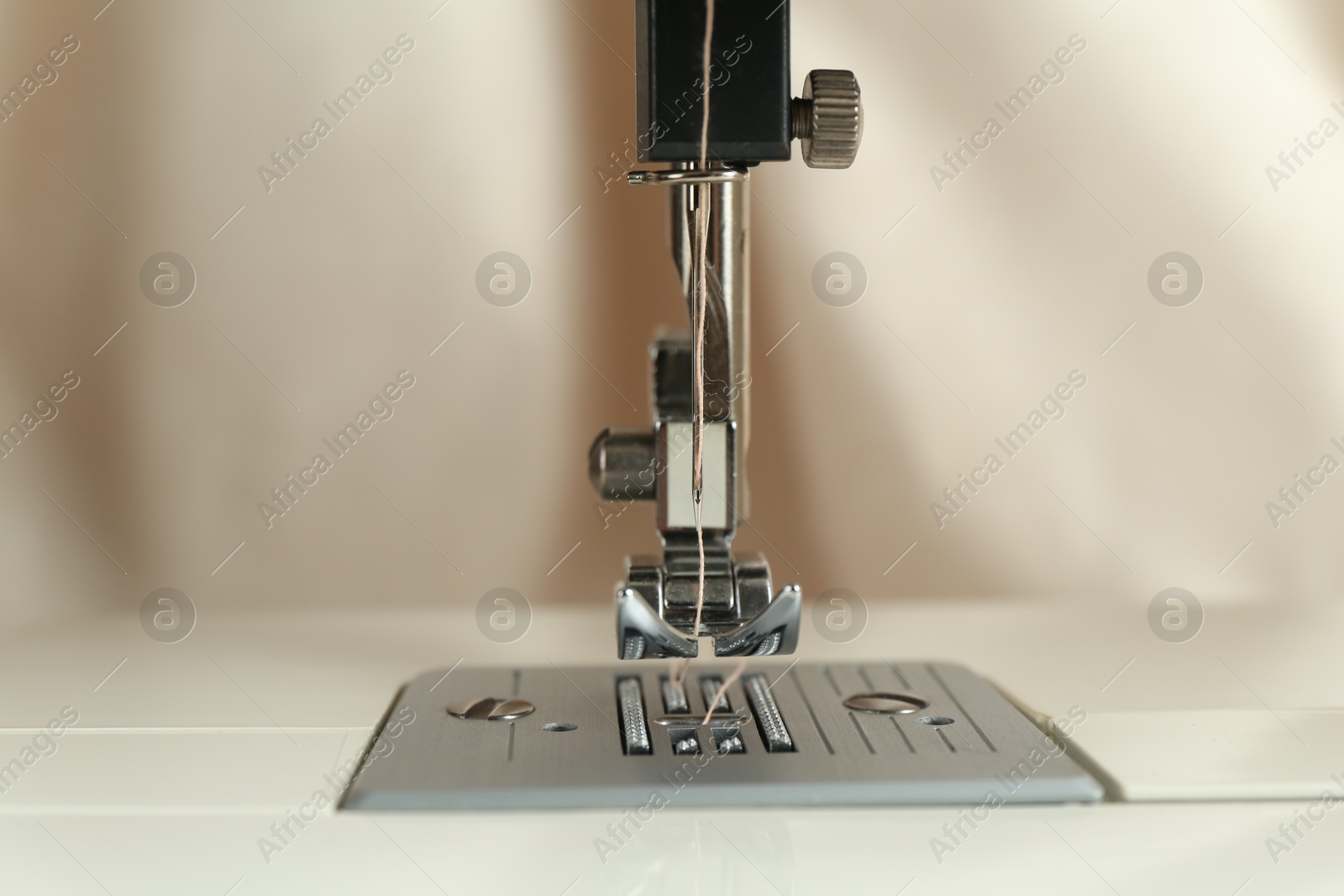 Photo of Sewing machine with beige thread on blurred background, closeup