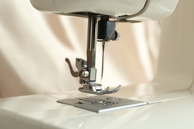 Photo of Sewing machine with beige thread on blurred background, closeup