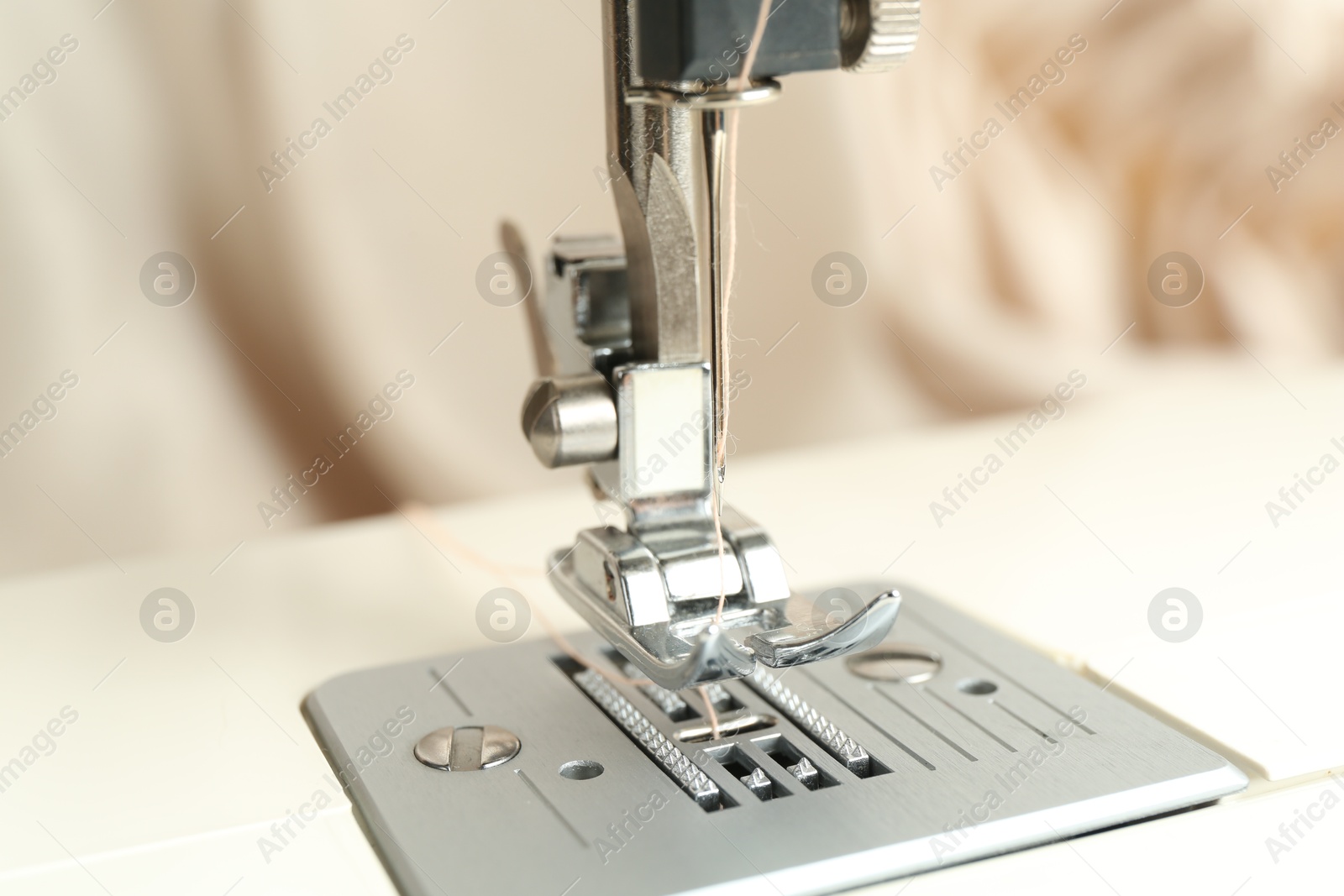 Photo of Sewing machine with beige thread on blurred background, closeup