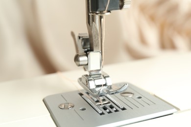 Sewing machine with beige thread on blurred background, closeup