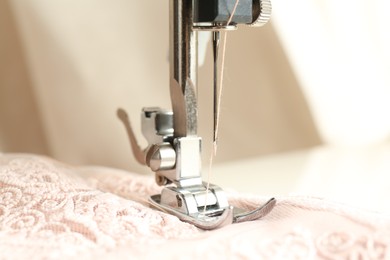 Sewing beige fabric with machine, closeup view