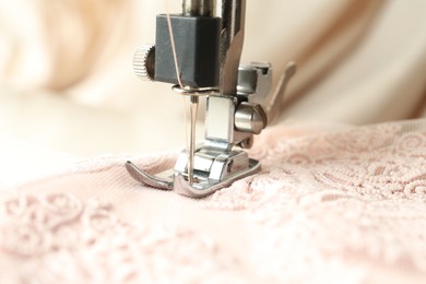 Photo of Sewing beige fabric with machine, closeup view