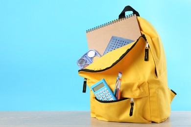 Photo of Backpack with different school stationery on wooden table against light blue background, space for text