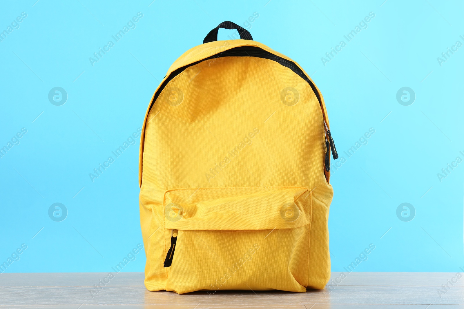 Photo of Yellow backpack on wooden table against light blue background