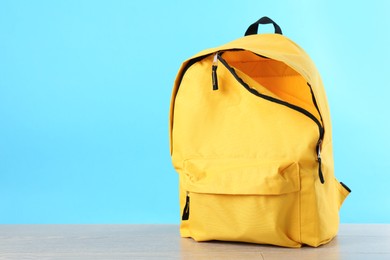 Photo of Yellow backpack on wooden table against light blue background, space for text