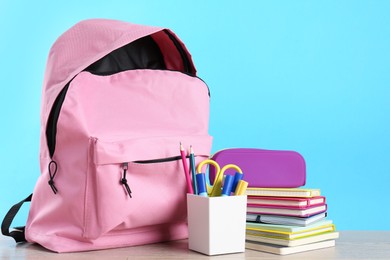 Photo of Backpack with different school stationery on wooden table against light blue background, space for text