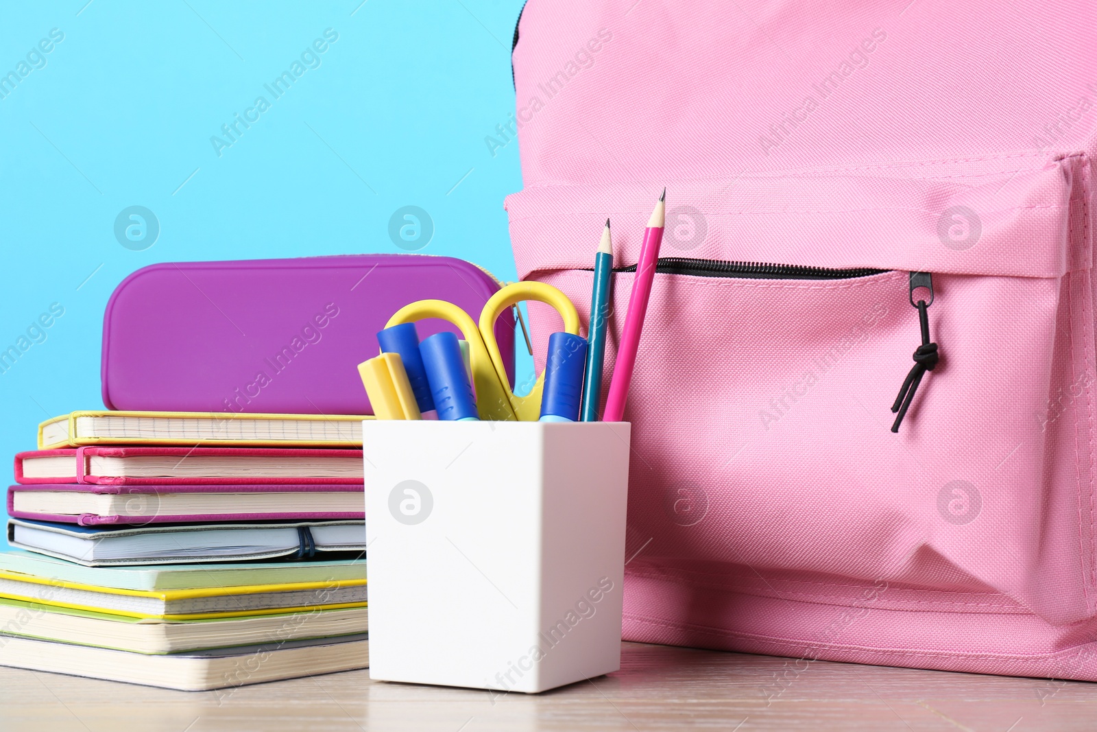 Photo of Backpack with different school stationery on wooden table against light blue background, closeup