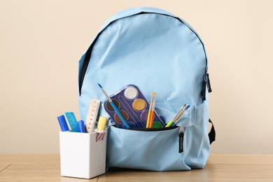 Photo of Backpack with different school stationery on wooden table against beige background