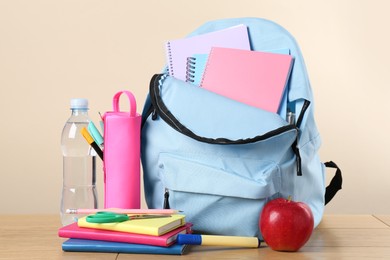 Backpack with different school stationery on wooden table against beige background