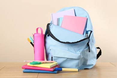 Backpack with different school stationery on wooden table against beige background