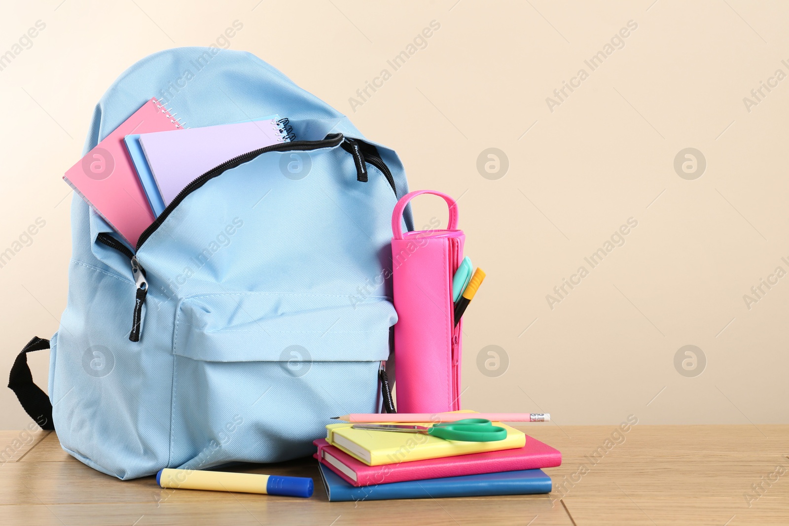 Photo of Backpack with different school stationery on wooden table against beige background, space for text