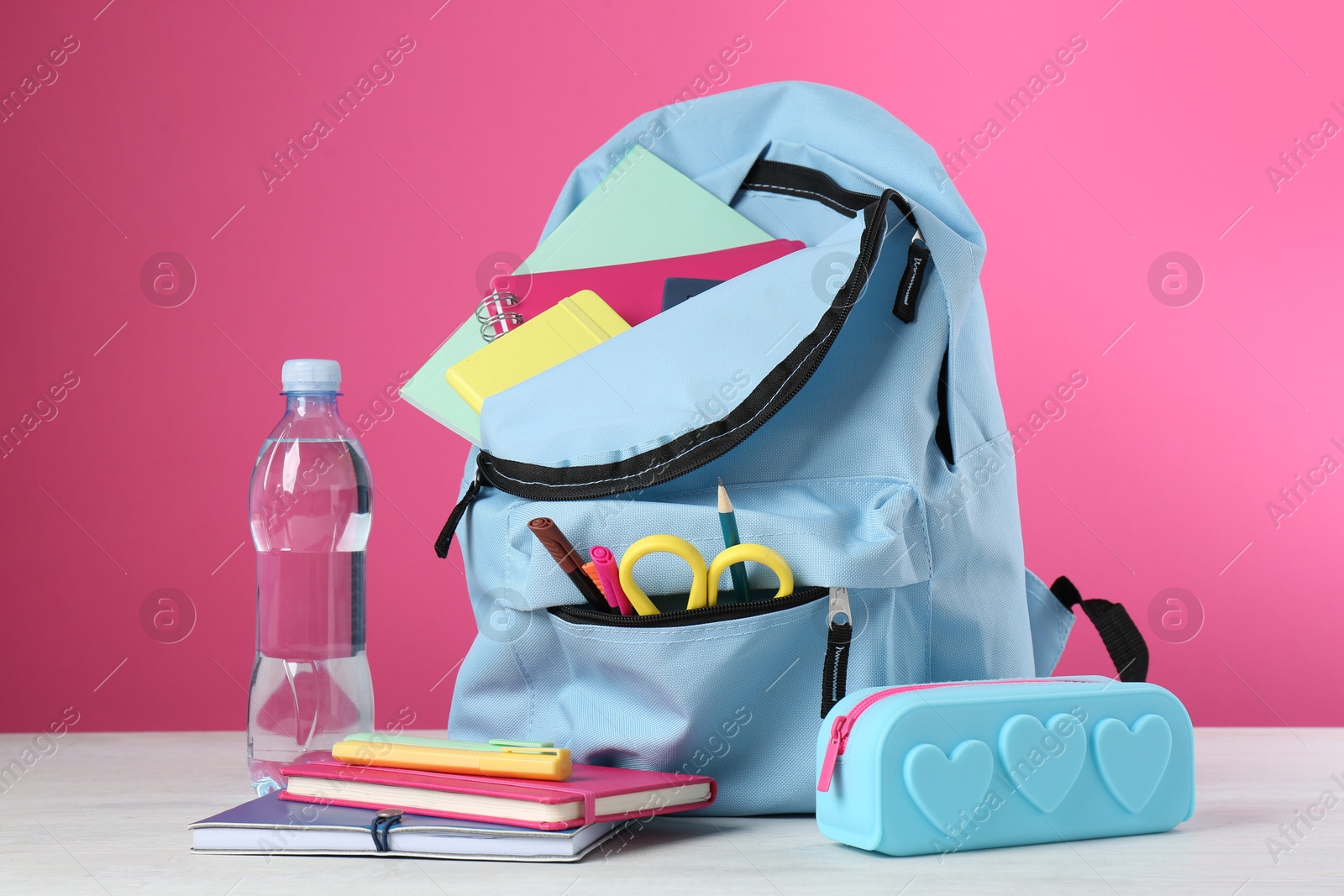 Photo of Backpack with different school stationery and bottle of water on light table against pink background