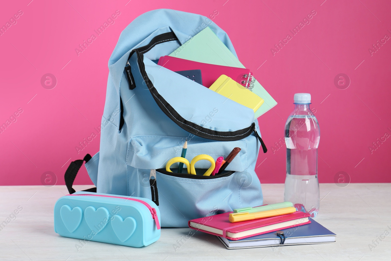 Photo of Backpack with different school stationery and bottle of water on light table against pink background