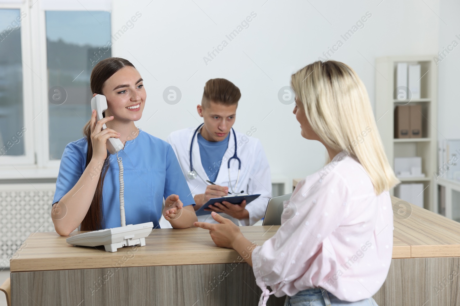 Photo of Professional receptionist and doctor working with patient at wooden desk in hospital