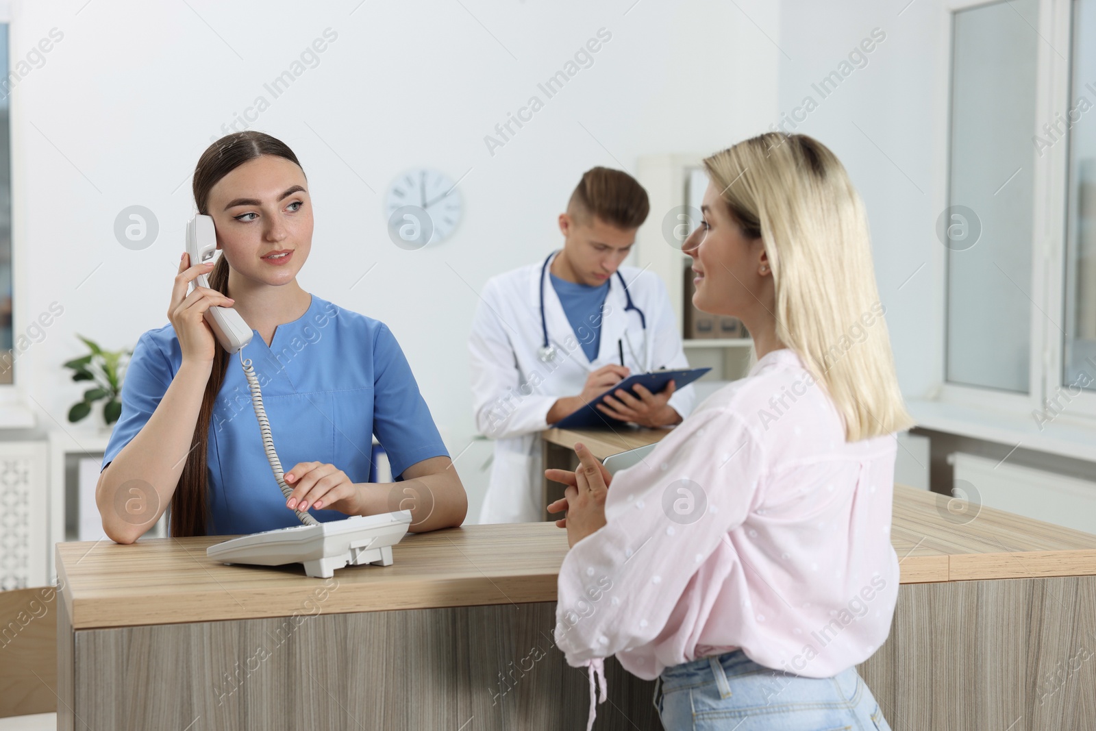 Photo of Professional receptionist and doctor working with patient at wooden desk in hospital