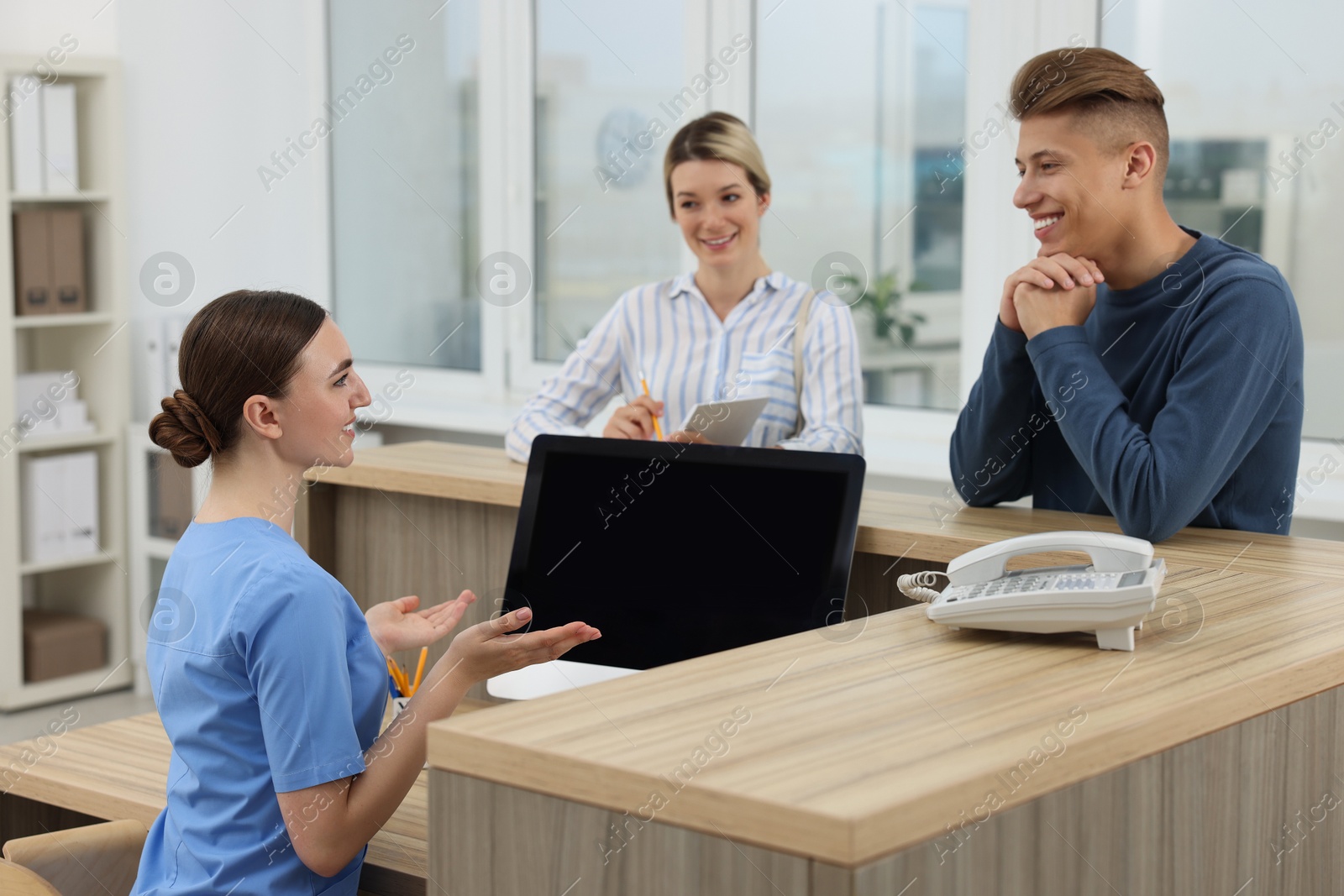 Photo of Professional receptionist working with patients at wooden desk in hospital