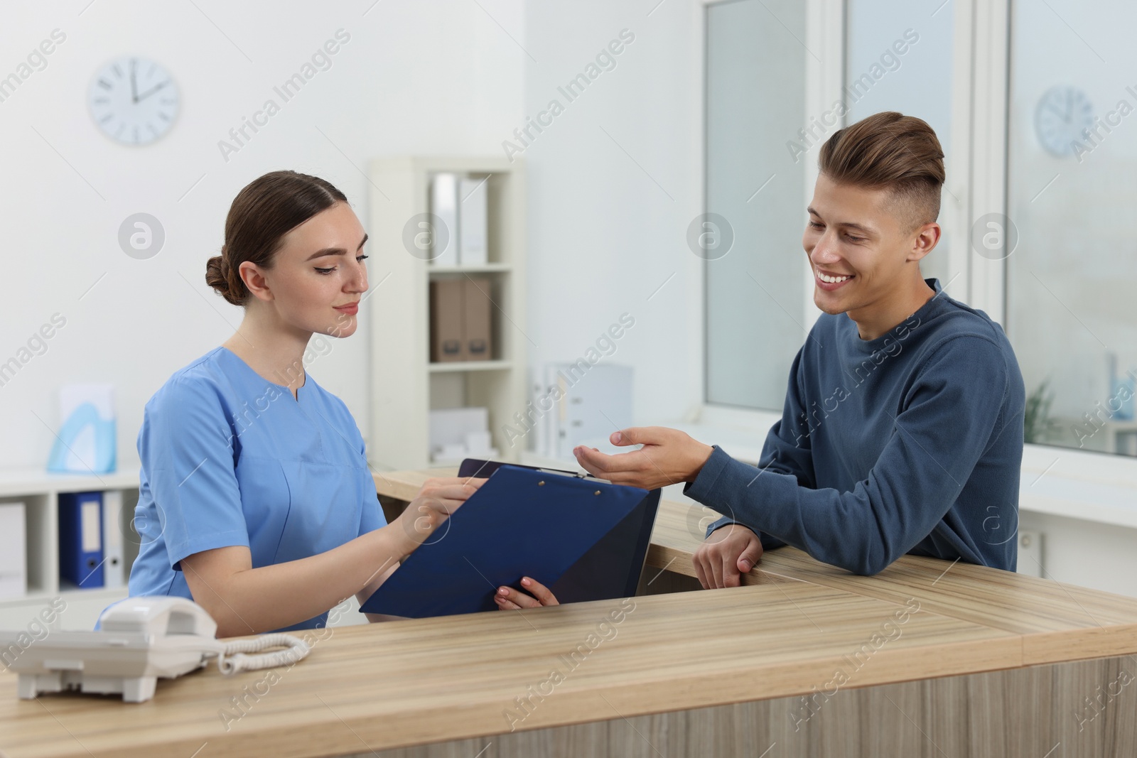 Photo of Professional receptionist working with patient at wooden desk in hospital