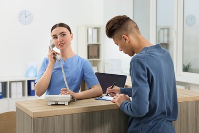 Professional receptionist working with patient at wooden desk in hospital