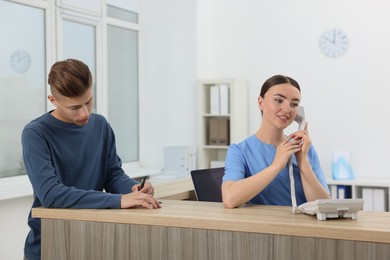 Professional receptionist working with patient at wooden desk in hospital