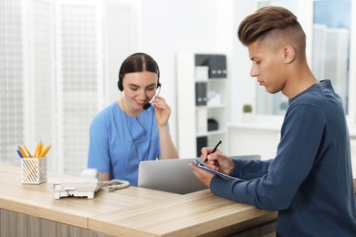 Photo of Professional receptionist working with patient at wooden desk in hospital