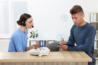 Professional receptionist working with patient at wooden desk in hospital