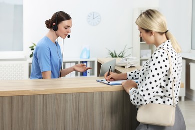 Professional receptionist working with patient at wooden desk in hospital