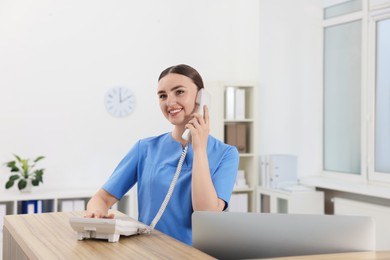 Professional receptionist talking on phone at wooden desk in hospital