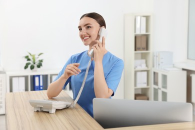 Photo of Professional receptionist talking on phone at wooden desk in hospital