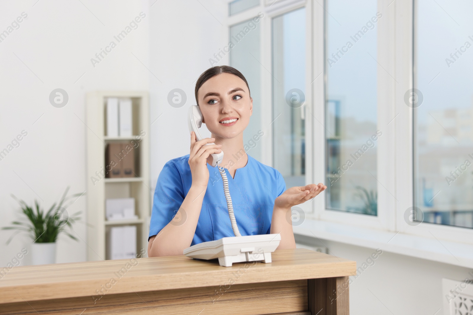 Photo of Professional receptionist talking on phone at wooden desk in hospital