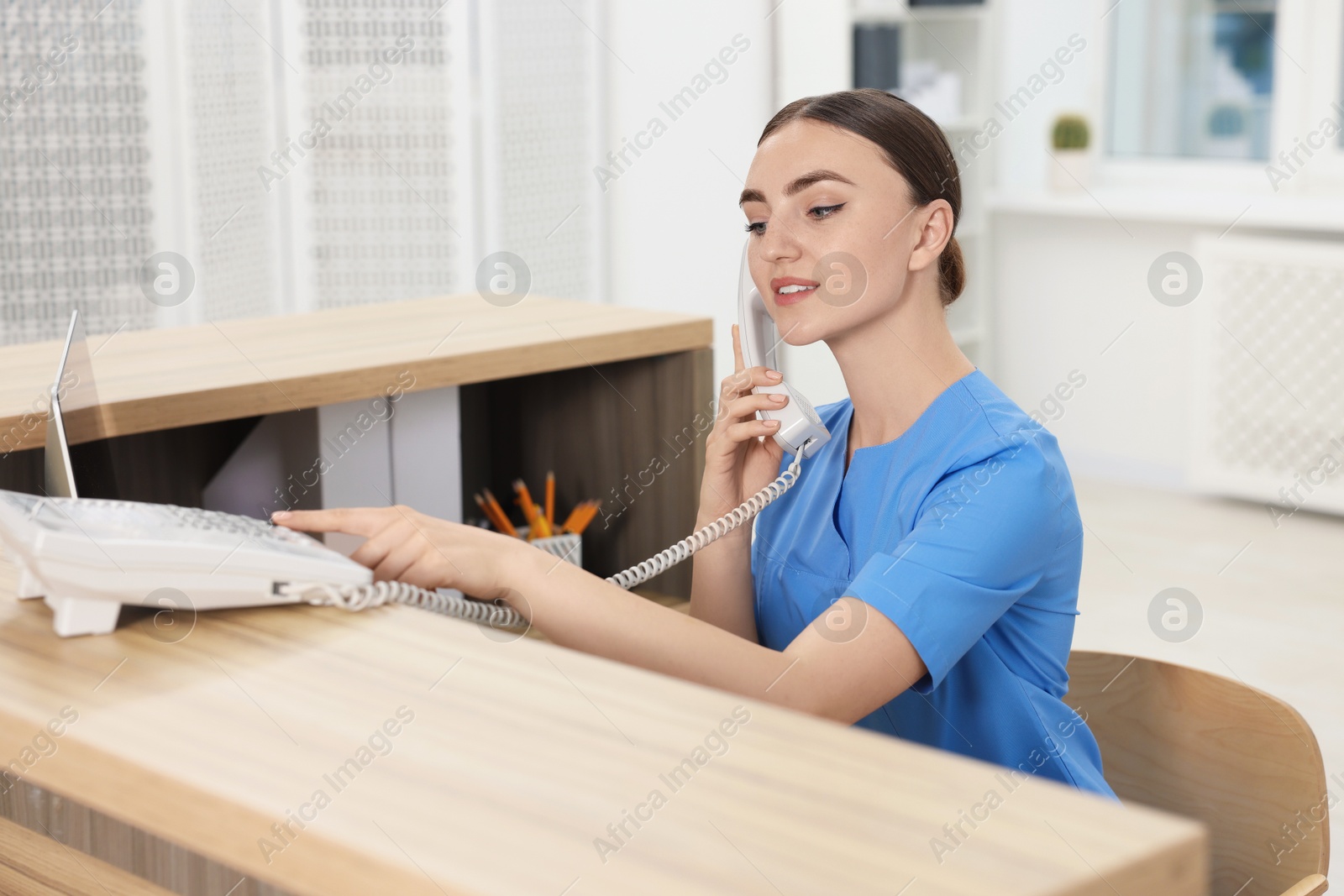 Photo of Professional receptionist talking on phone at wooden desk in hospital