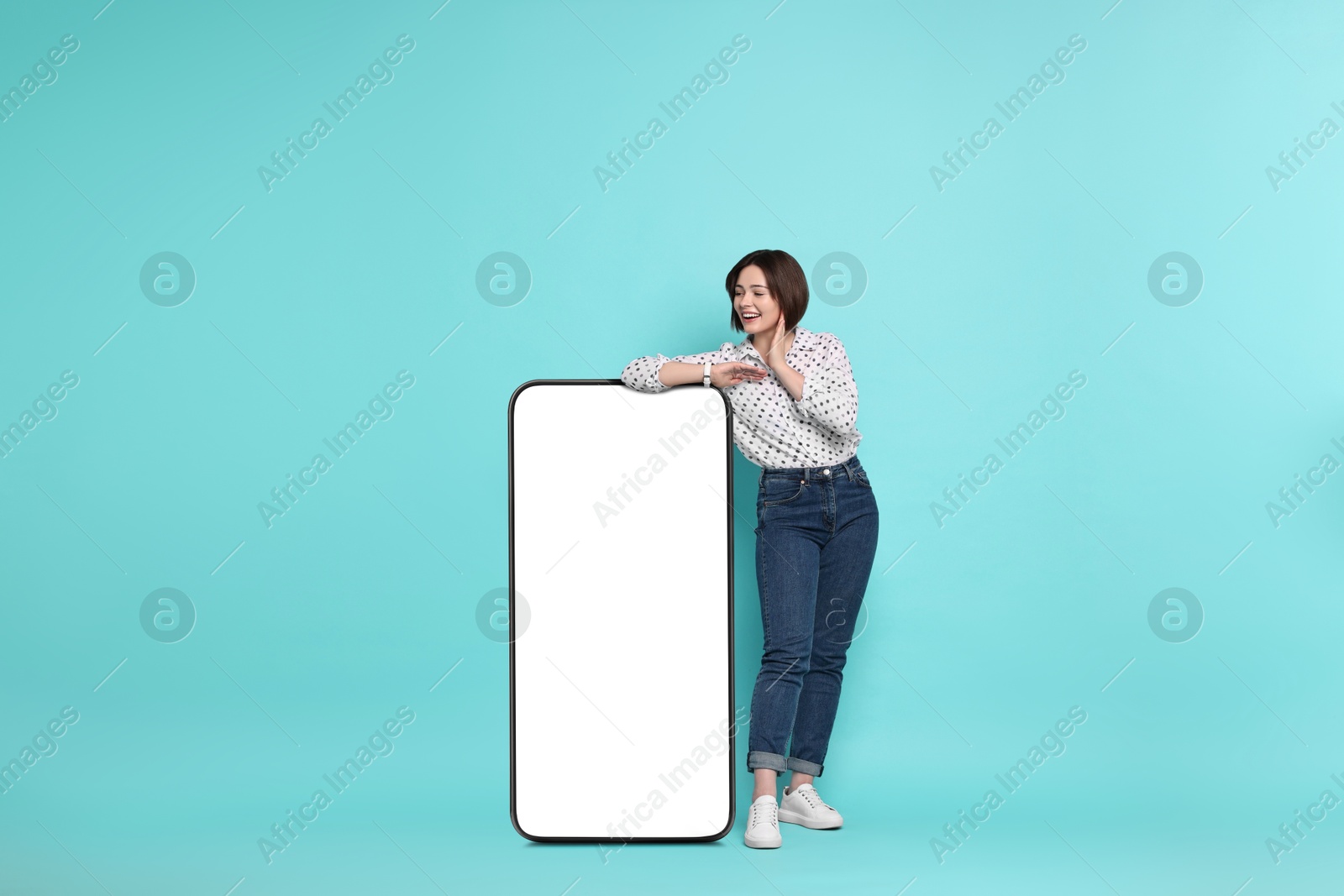 Image of Beautiful young woman leaning on big mobile phone with blank screen against turquoise background