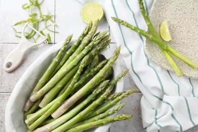 Photo of Fresh green asparagus stems, lime and vegetable peeler on light textured tiled table, flat lay