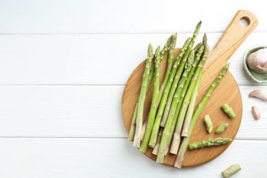 Photo of Fresh green asparagus stems and garlic on white wooden table, flat lay. Space for text