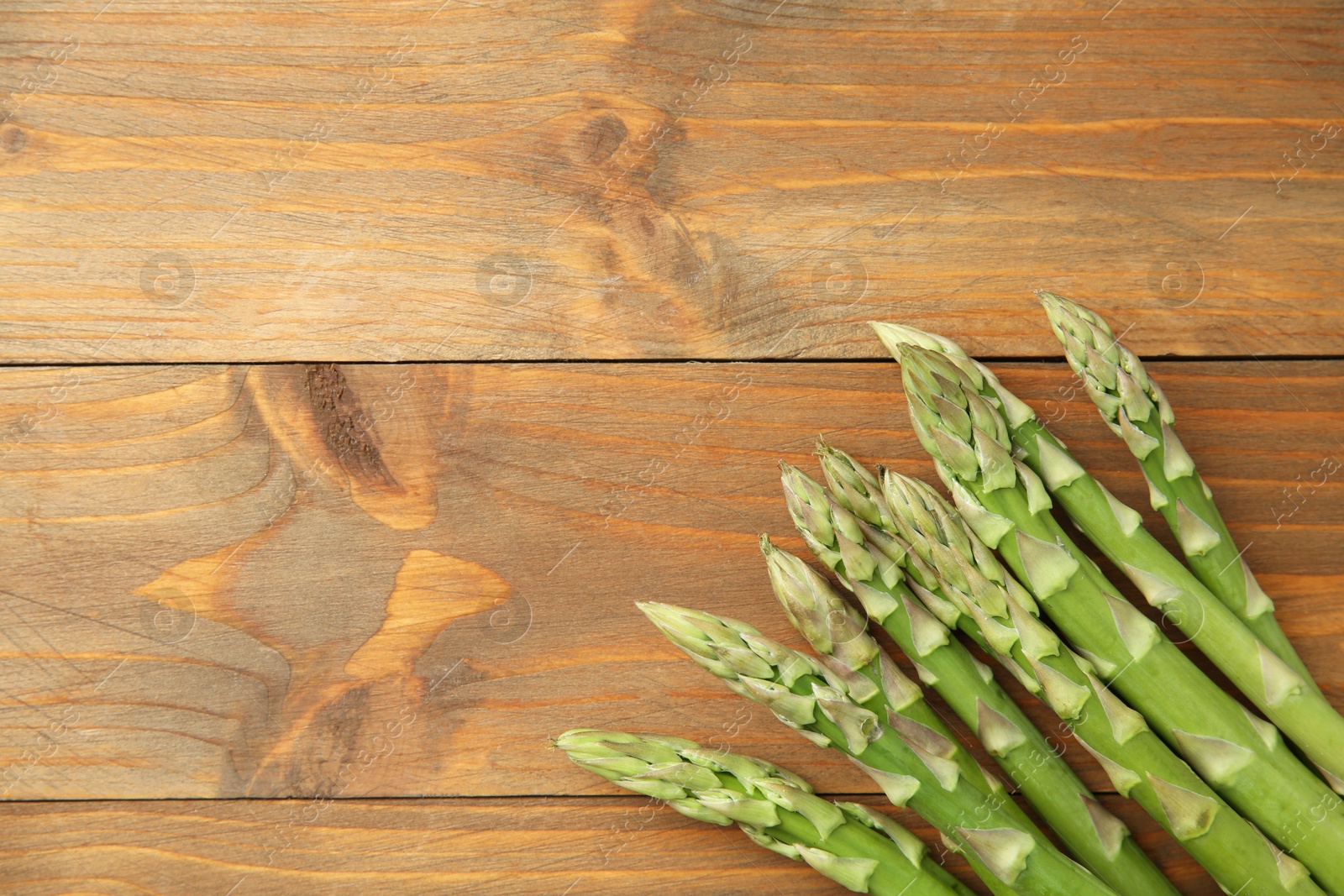 Photo of Fresh green asparagus stems on wooden table, top view. Space for text