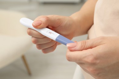 Woman holding negative pregnancy test indoors, closeup view