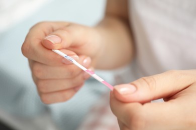 Woman holding pregnancy test indoors, closeup view